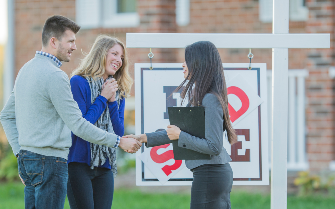 Couple shaking hands with a realtor in front of a house for sale