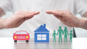 Man with his hands over a house, car and people to signify insurance